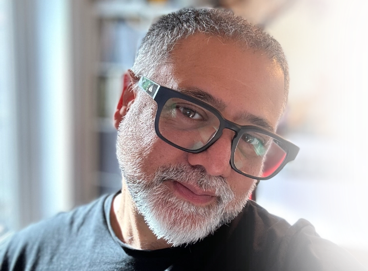 Mani wearing glasses with a blurred indoor background